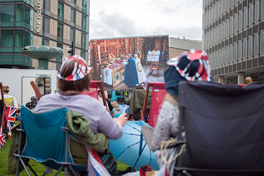 Des spectacteurs regardent le couronnement sur une place publique.  