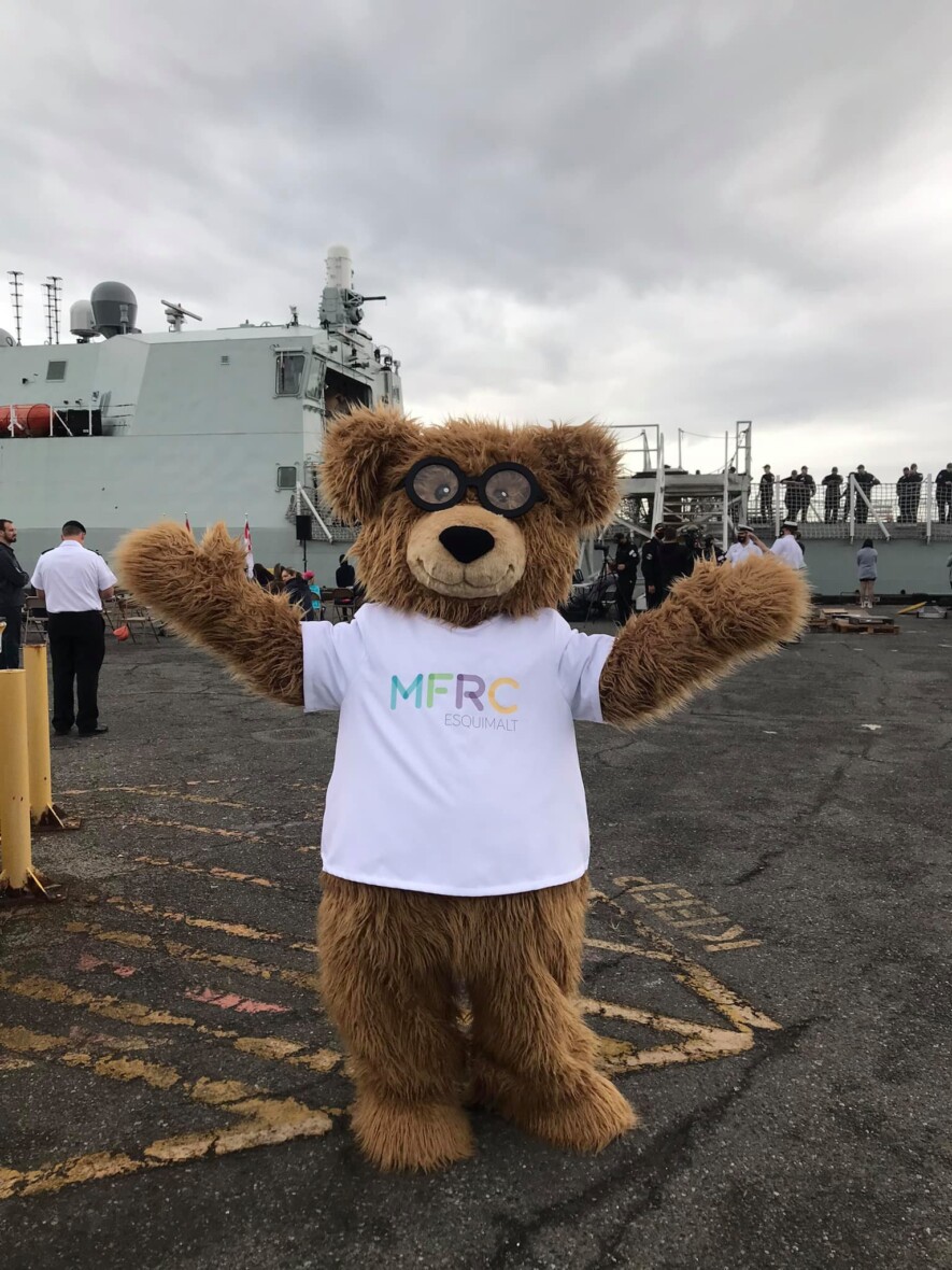 La mascotte du Centre de ressources pour les familles des militaires d’Esquimalt devant un bateau des Forces armées canadiennes | courtoisie   